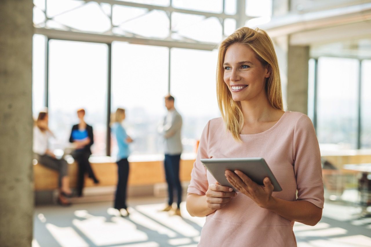 Mujer sonriendo mientras sostiene una tablet con canales digitales de atención al cliente